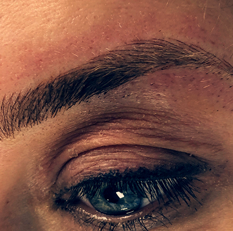 Hair-stroke microblading detail on blue-eyed client